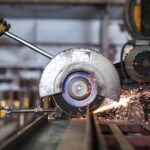 A person with a glove that has a dollar sign on it grips a circular saw in a machine shop.